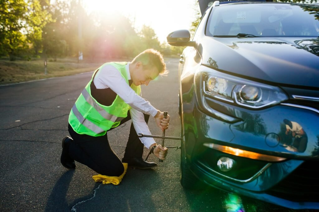 A man in a green safety vest changes a flat tire on a road.